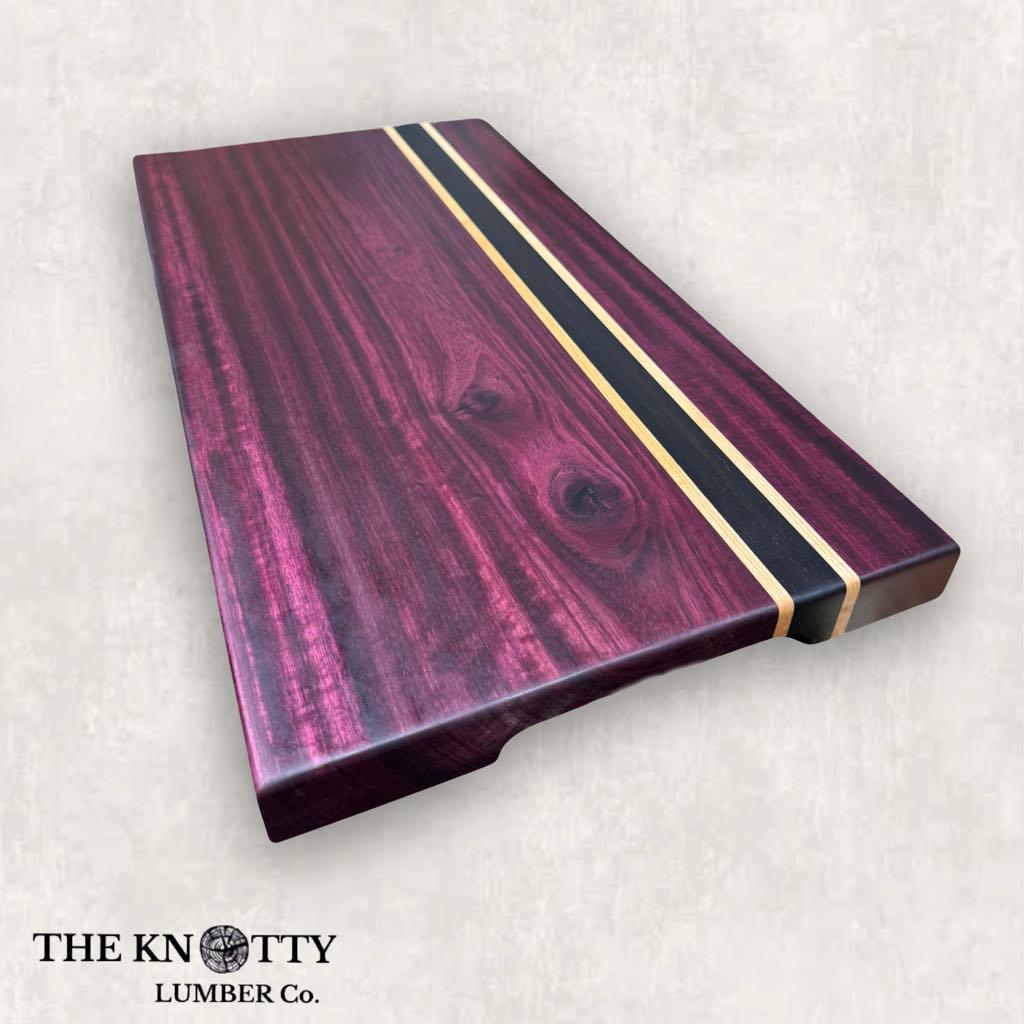 A assembled cutting board made of purpleheart wood with Wenge and Maple strips, branded by THE KNOTTY LUMBER CO.