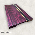 A assembled cutting board made of purpleheart wood with Wenge and Maple strips, branded by THE KNOTTY LUMBER CO.