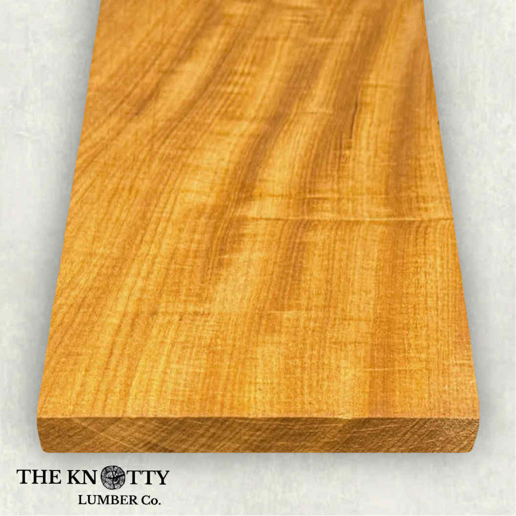 African teak afromosia hardwood board with visible grain texture on a white background, branded 'The Knotty Lumber Co'.