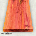 Aromatic cedar pink and red wood board with visible grain pattern on a light background, branded 'The Knotty Lumber Co'.