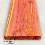 Aromatic cedar pink, red, and white wood board with visible grain pattern on a light background, branded 'The Knotty Lumber Co'.