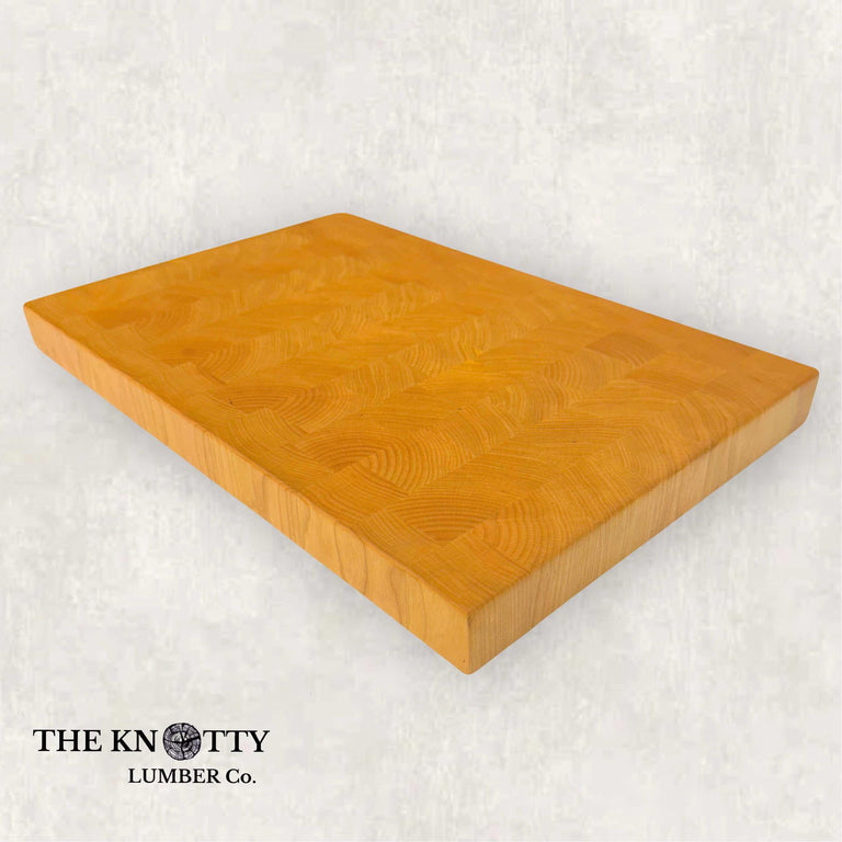 A rectangular end grain cherry wood butcher block with a smooth finish. The wood has natural variations in color, and the block is branded with 'The Knotty Lumber Co.