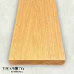 Red oak wood board with visible grain patterns on a grey background. branded with 'The Knotty Lumber Co'