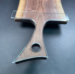 A close-up of a wooden serving board or cutting board with a clear acrylic guide or insert placed along the top edge, photographed on a dark gray surface.