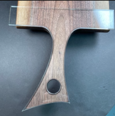 A close-up of a wooden T-shaped tool or handle with a circular hole near the base, shown on a dark gray surface.